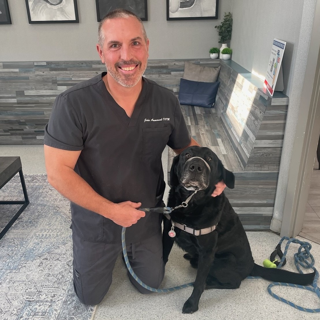 A man in scrubs kneels beside a black dog